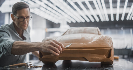 Portrait of an Automotive Artist Making Final Strokes on His Latest Concept Car Creation. Designer Working on a New Prototype, Sculpting Industrial Plasticine Clay 3D Model of a Sport Coupe.