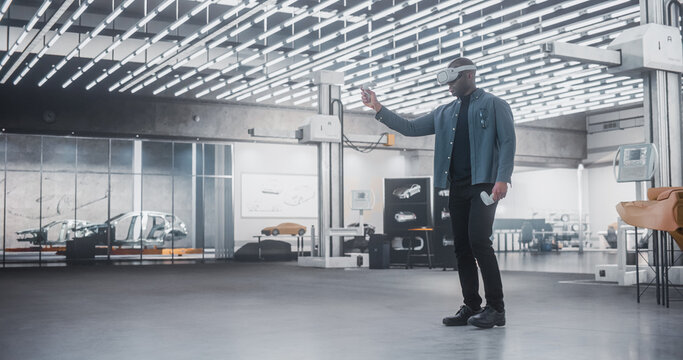Black Male Car Designer Wearing a Virtual Reality Headset and Using Controllers to Work on a Concept Car Or Aerodynamics. Talented Design Professional Working in VR Set to Analyze And Test the Vehicle - Powered by Adobe