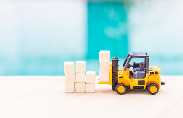 Miniature worker in safety suite on forklift truck and wooden cubes, cargo industry concept