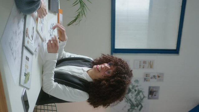 Female interior designer showing furniture catalog and speaking with client in the office while presenting project during meeting. Vertical format footage