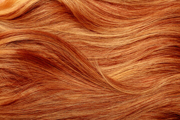 Red hair close-up as a background. Women's long orange hair. Beautifully styled wavy shiny curls. Hair coloring bright shades. Hairdressing procedures, extension.