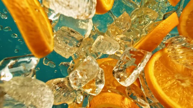 Citrus orange slices and ice cube fly or fall on blue background, slow motion vertical or horizontal. Fresh juicy orange and juice, ice cube and water drops splash pours in super slow motion 1000 fps