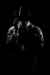 A dark silhouette of a man in a coat and hat in the noir style. A dramatic portrait in the style of...