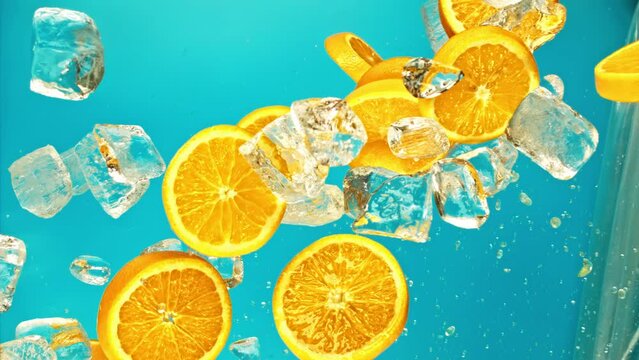Fresh juicy orange and juice, ice cube and water drops splash pours in super slow motion 1000 fps. Citrus orange slices and ice cube fly or fall on blue background, slow motion vertical video 1000fps