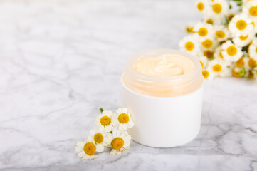 Obraz na płótnie Canvas Open jar of moisturizing cream for face, body and hands with a chamomile flower on a light background. Herbal dermatological cosmetic hygiene cream. Natural cosmetic product. Beauty concept. MOCKUP
