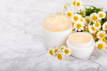 Fototapeta na wymiar Open jar of moisturizing cream for face, body and hands with a chamomile flower on a light background. Herbal dermatological cosmetic hygiene cream. Natural cosmetic product. Beauty concept. MOCKUP
