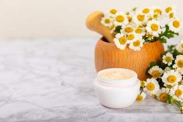 Fototapeta na wymiar Open jar of moisturizing cream for face, body and hands with a chamomile flower on a light background. Herbal dermatological cosmetic hygiene cream. Natural cosmetic product. Beauty concept. MOCKUP