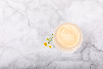 Open jar of moisturizing cream for face, body and hands with a chamomile flower on a light background. Herbal dermatological cosmetic hygiene cream. Natural cosmetic product. Beauty concept. MOCKUP