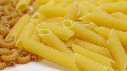 tas de pâtes penne et de coquillettes au blé complet cru, en gros plan, isolé sur un fond blanc
