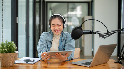 A cheerful Asian female radio host speaking into a microphone, and recording her podcast - obrazy, fototapety, plakaty