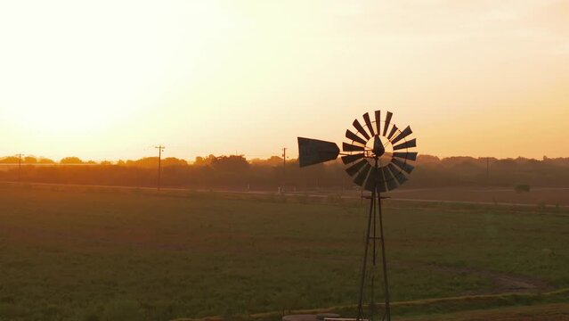 A vintage windmill stands in the foreground in Texas at sunrise.