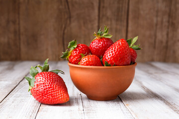Large berries of organic strawberries in a clay ceramic bowl on a wooden background.