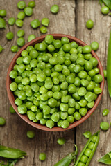 Green peas in closed and open pods, peeled peas in a bowl, scattered pea seeds on a wooden background, top view