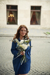 Fototapeta premium Smiling, positive emotions. Beautiful woman is with flowers in hands outdoors