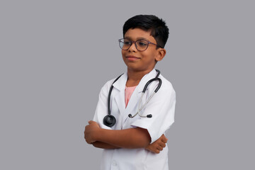 Indian Asian kid boy aged 7 to 8, wearing a doctor apron with stethoscope. standing and folding...