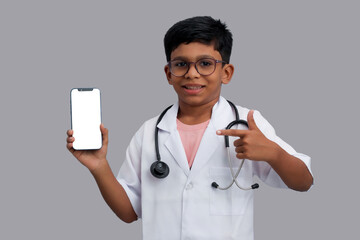 Indian Asian kid boy aged 7 to 8, wearing a doctor apron with stethoscope. standing with smartphone...