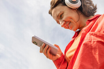 View from bottom. Woman using mobile phone and headphones outdoor