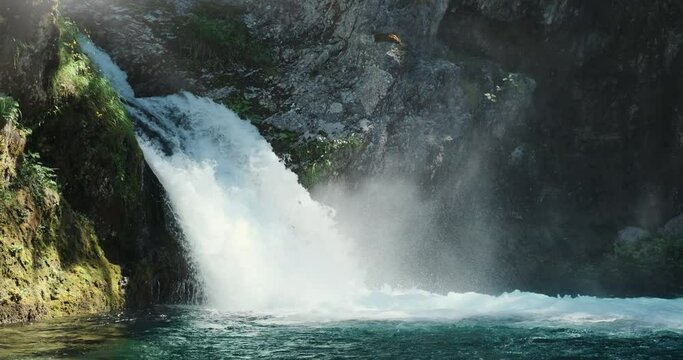 Beautiful waterfall in magic sun morning light. 4k static video. Blue clear water of mountain river fall from rock in spring forest, side view. Blue Eye waterfall. Scenic Albania. Green clean nature