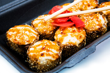 Baked sushi roll in soy sauce with ginger and chopsticks. Takeaway food.
