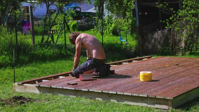 Deck construction, builder hand with electric screwdriver installing impregnated wooden boards