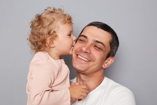 Cheerful smiling young man holding little baby girl isolated on gray background infant kid kissing father expressing love and happiness joyful family