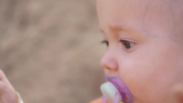 baby baby close-up with a pacifier in his mouth. happy family kid dream concept. baby boy portrait outdoors eyes close-up. baby face sitting on the sand looking lifestyle away
