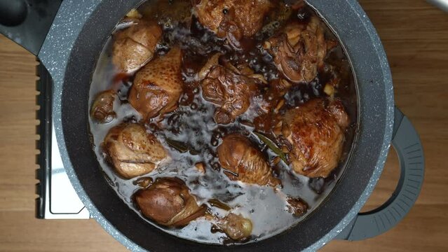 Chicken pieces simmering in liquid dark sauce while reducing the sauce.