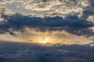 Yellow light of the Sun comes out of the dark blue clouds in the sky on a cloudy day