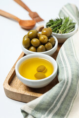Olive branches, oil and olives in bowls, towel on white background, top view