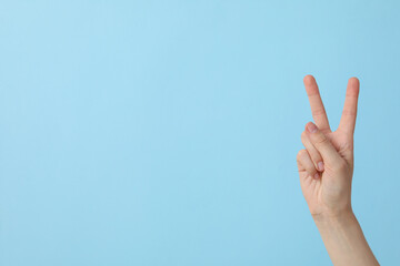 Female hand showing two fingers on a blue background, place for text