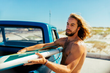 Young male surfer getting his surf board out of a truck bed and getting ready to surf