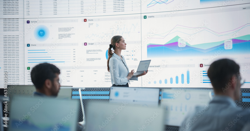 Poster Female Data Scientist Using Laptop And Analyzing Information And Graphs On Big Digital Screen In Monitoring Office. Caucasian Woman Working For Big Data Company, Diverse Employees Behind Computers.