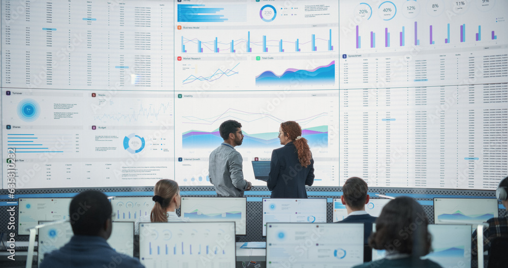 Poster Back View Of Indian Data Analyst And Hispanic Manager Discussing Reports On Digital Screen in Monitoring Room. Male and Female Experts Talking, Employees Working On Computers In Consulting Company