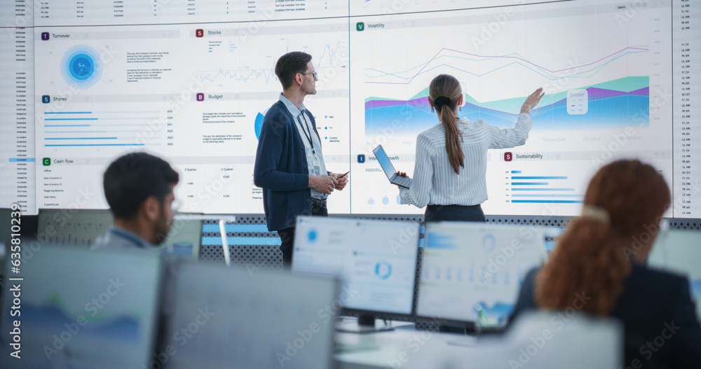 Poster Female Data Scientist And Male Project Manager Discussing Reports And Graphs On Big Digital Screen In Monitoring Office. Diverse Employees Working Behind Computers in Artificial Intelligence Company.