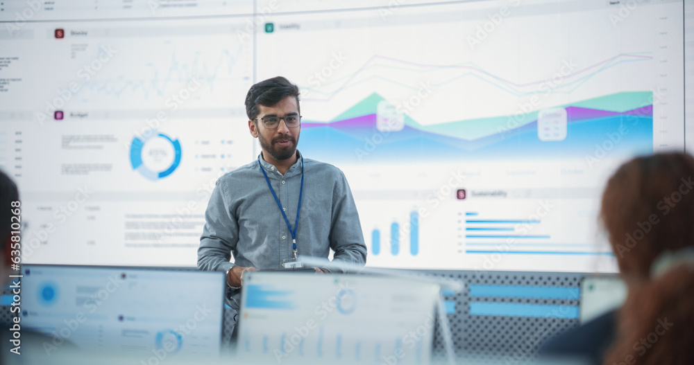 Poster Male Indian Computer Scientist With Tablet Giving Presentation to Diverse Team Of Data Analysts In Front Of Big Digital Screen In Monitoring Room. Colleagues Listening To Training On Automation.