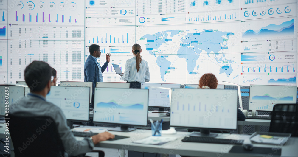 Aufkleber Back View Of Black Male Analyst Talking To Caucasian Female Manager In Front Of Big Digital Screen With World Map In Monitoring Office. Diverse Employees Working Behind Computers In Logistics Company.
