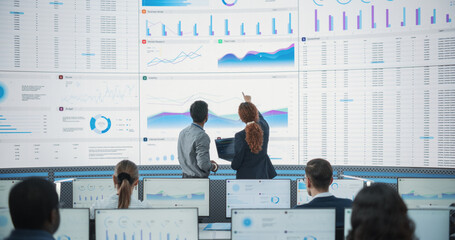 Wide Zoom In Back Shot Of Diverse Male And Female Risk Managers Analyzing Data On Digital Screen In Monitoring Room. Multiethnic Employees Working On Computers For Succesful Venture Capital Company