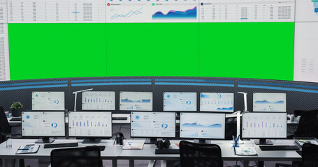 Empty Monitoring Office With Green Screen Chromakey On Big Digital Screen. Desktop Computer Monitors Of Employees Showing Graphs And Charts. Mockup Template Of Successful Financial Analytics Company.