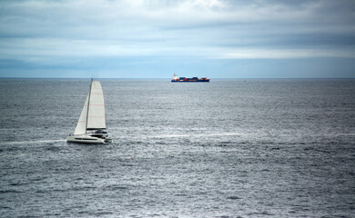 Sailboat and cargo ship among the waves on the high seas