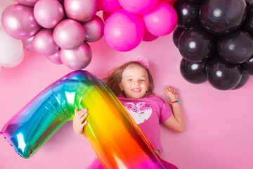 Obraz na płótnie Canvas Portrait of a happy little girl lying on a pink background with balloons. and holding the number 7. Happy birthday. Pink background.