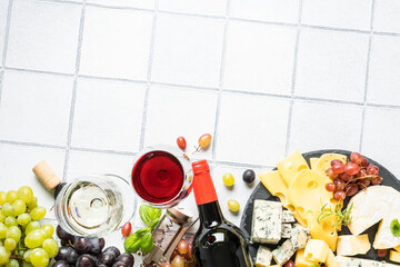 Wine set with Craft cheese assortment and fresh grape at white tile background. Flat lay with space for text.