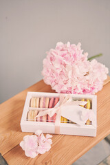 Dessert French Macarons in present box. Sweet dessert on a flowers background. Still life with macaroni cakes and different flower. Delivery concept, coffee and flower shop