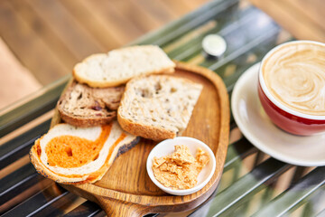Assorted sliced bread on a wooden board. Served with smoked butter. Breakfast with cappuccino coffee. Composition with butter and bread on wooden plate.