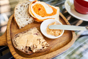 A slice of bread with butter on a chopping board. Assorted sliced bread on a wooden board. Served with smoked butter. Breakfast with cappuccino coffee. 