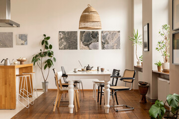 Living room of dining room interior with mock up poster frame, stylish table, rattan chair, wooden kitchen island, white chocker, plants, kitchen hood and personal accessories. Home decor. Template.