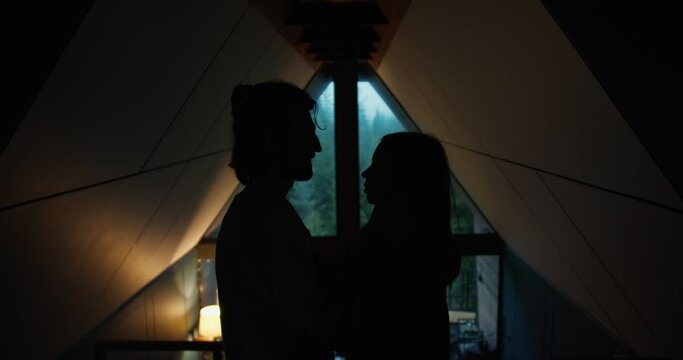Happy silhouettes in a house with a triangular roof, a guy and a girl are hugging and standing close to each other in a dark room