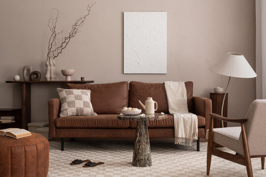 Creative composition of cozy living room interior with mock up poster frame, brown sofa, stylish lamp, chess prints carpet, coffee table, boucle armchair and personal accessories. Home decor. Template
