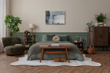 Creative composition of bedroom interior with mock up poster frame, green bedding, wooden side table, stylish bench, beige rug, plants, basket, lamp and personal accessories. Home decor. Template.