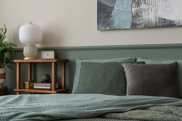 Minimalist composition of bedroom interior with mock up poster frame, bed, green bedding, wooden sideboard, stylish lamp, clock and personal accessories. Home decor. Template.