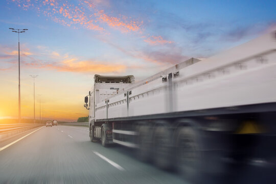 Truck with an open trailer and concrete building materials drives motion blur effect speed along highway in heavy traffic in the with clouds in the sunset sky.